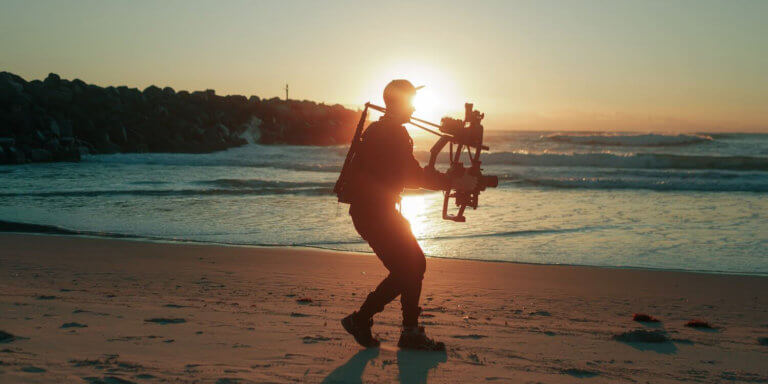 Creative director filming on a beach to represent cloud-bsaed post-production